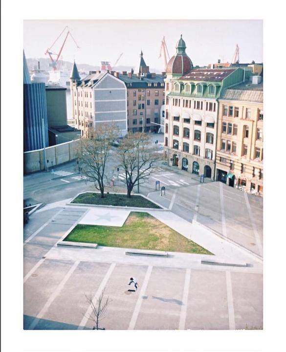 A high-angle view shows a city square with buildings and cranes in the background.