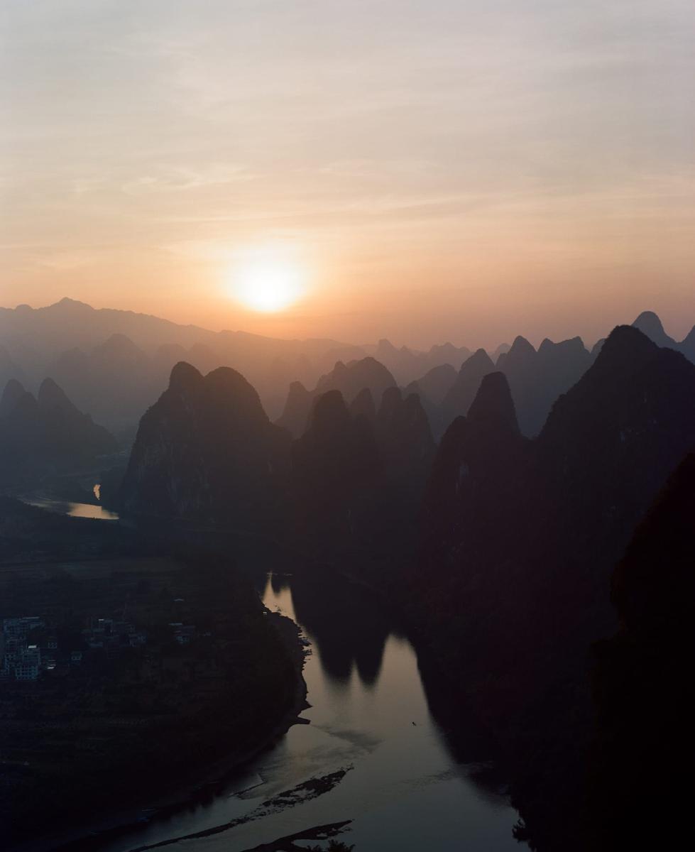 The sun sets over a river winding through a valley of karst mountains.