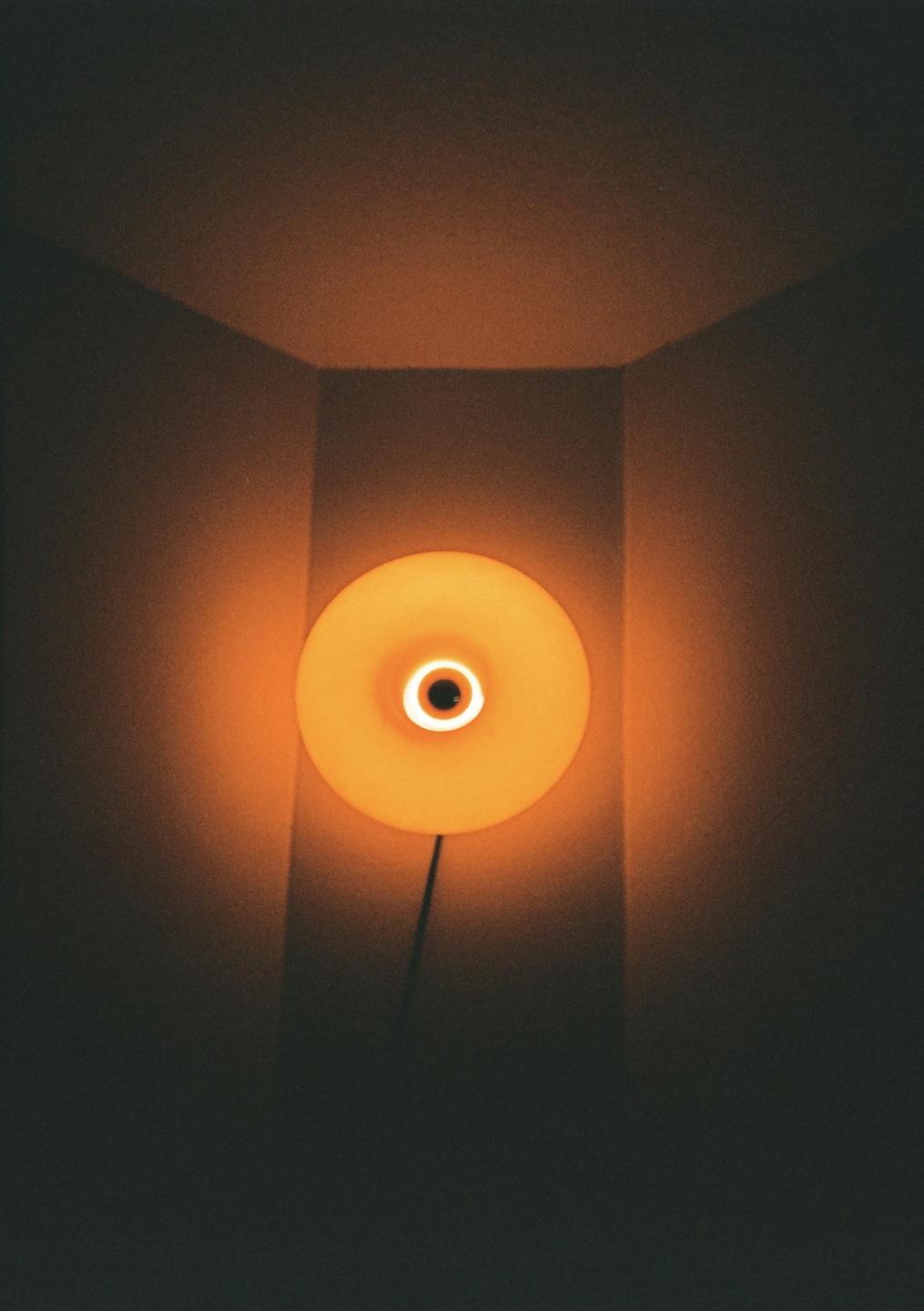 A circular orange light fixture is mounted on a wall in a corner, casting a warm glow.