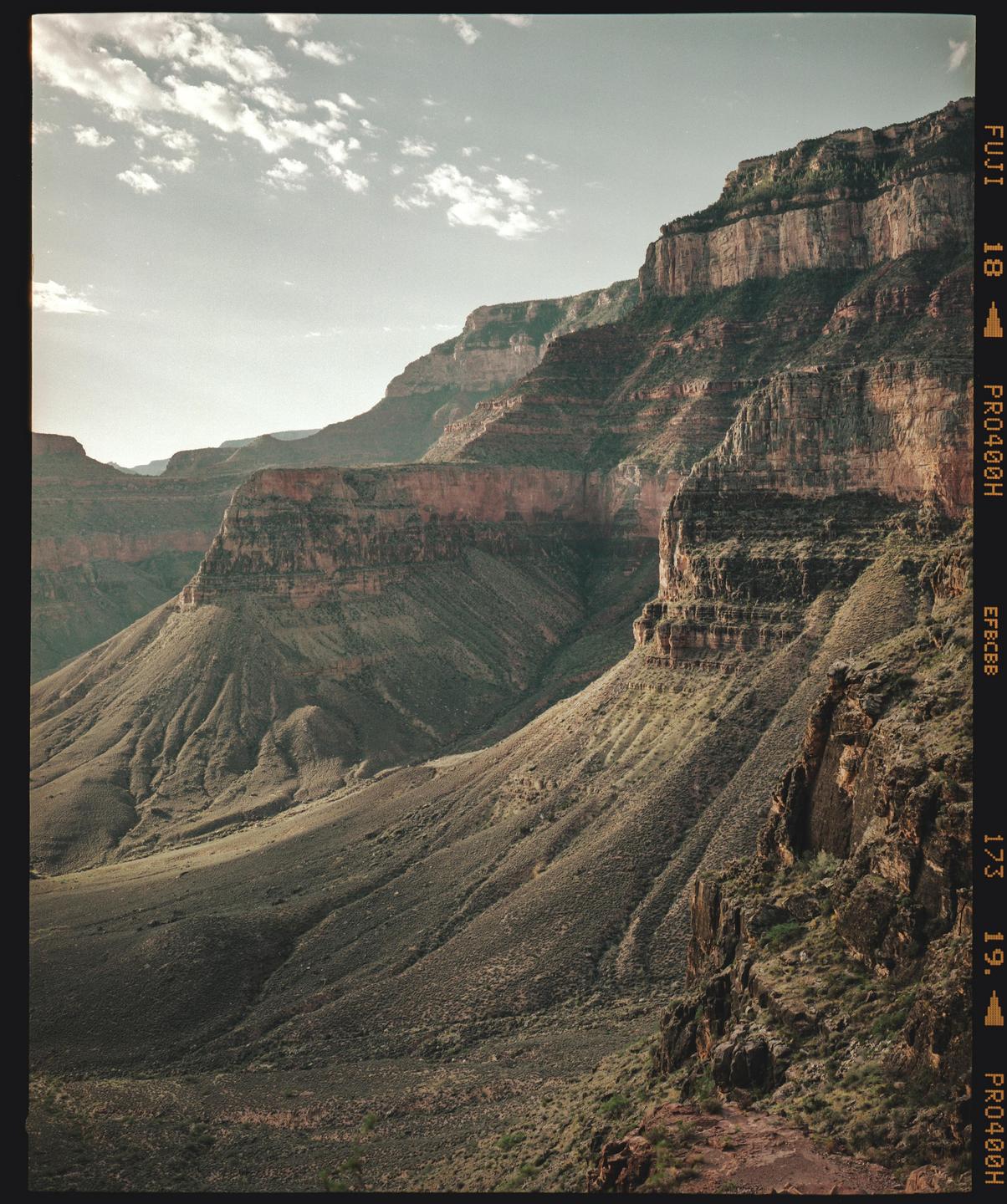 A vast canyon landscape features steep, rocky slopes and a cloudy sky.