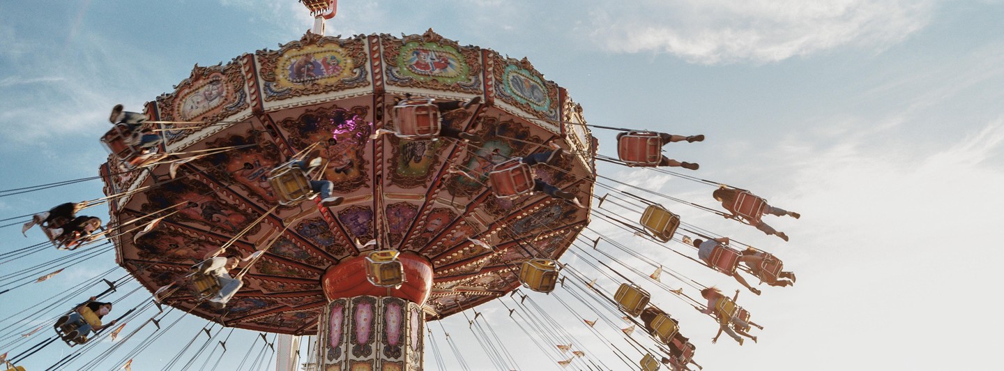 People ride a swing carousel at a fair against a bright sky.