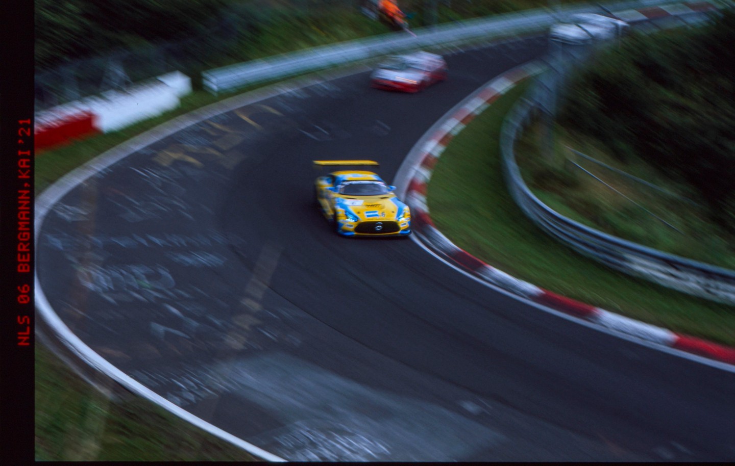 A yellow and blue race car speeds around a track with another car in the distance.