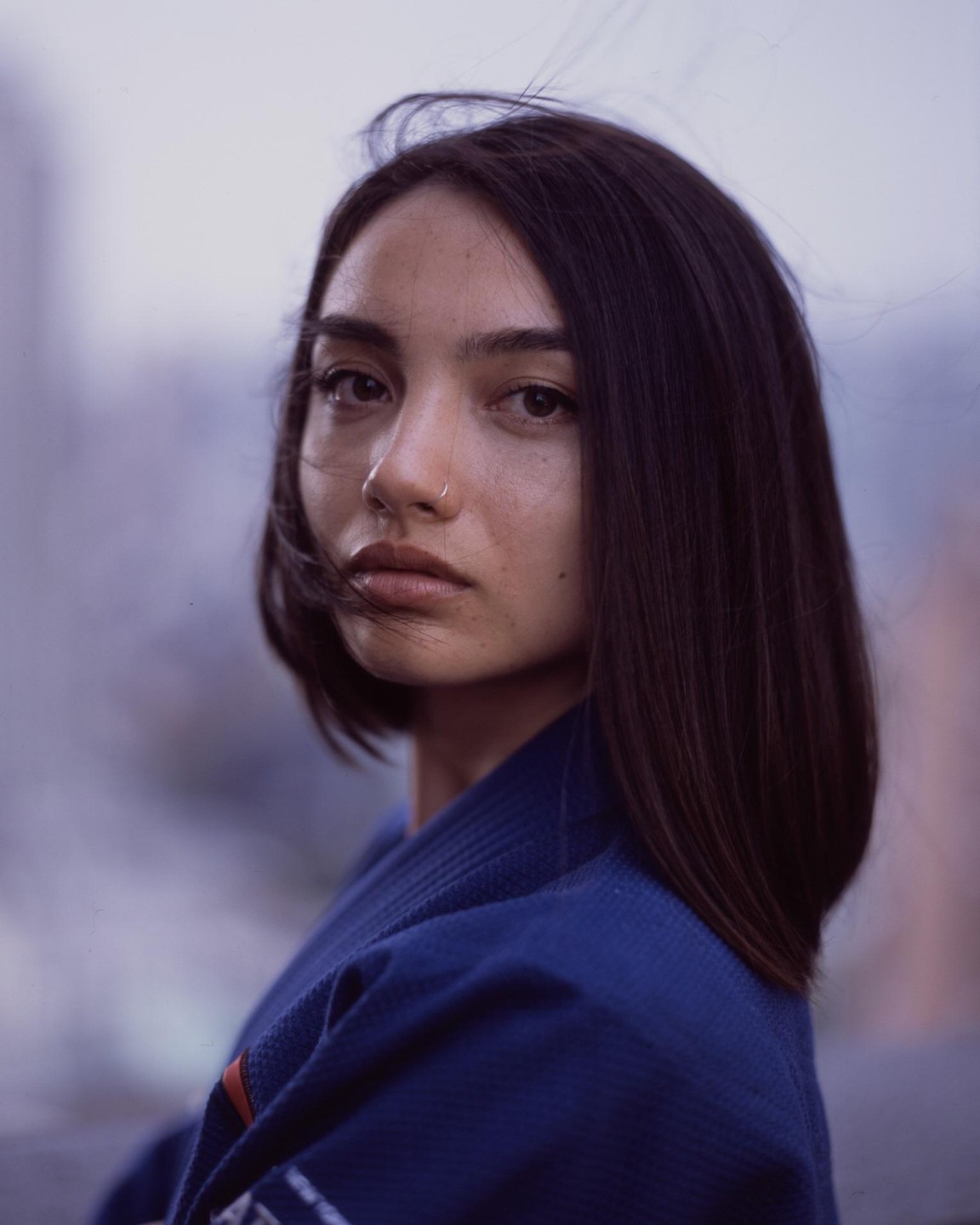 A woman with dark hair and a nose ring looks directly at the viewer.