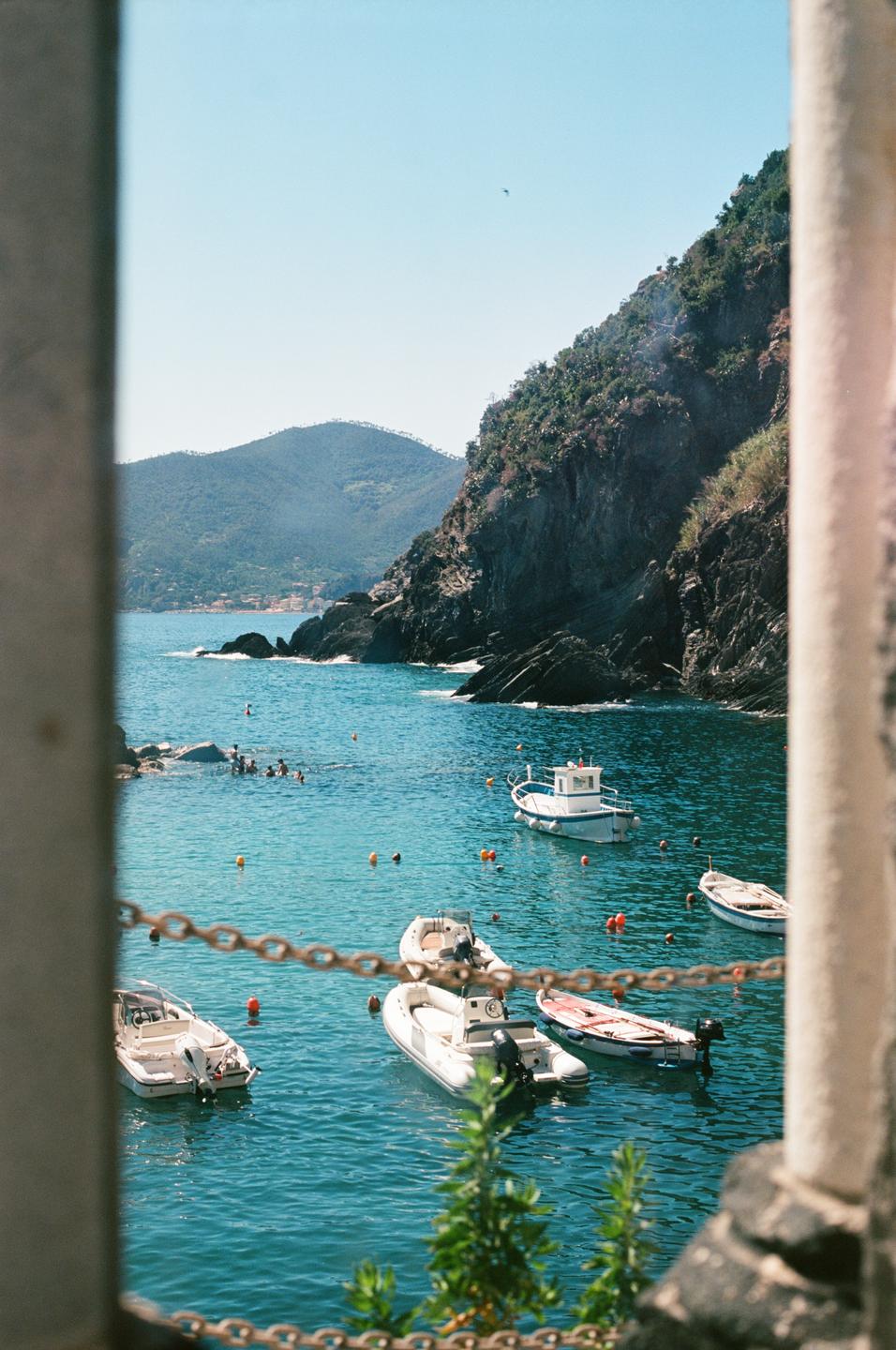 Boats float in the clear blue water of a cove surrounded by mountains.