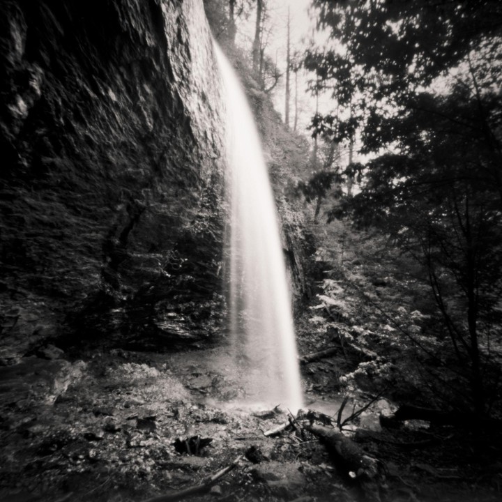 A long exposure captures a waterfall cascading down a rocky cliff into a forest.