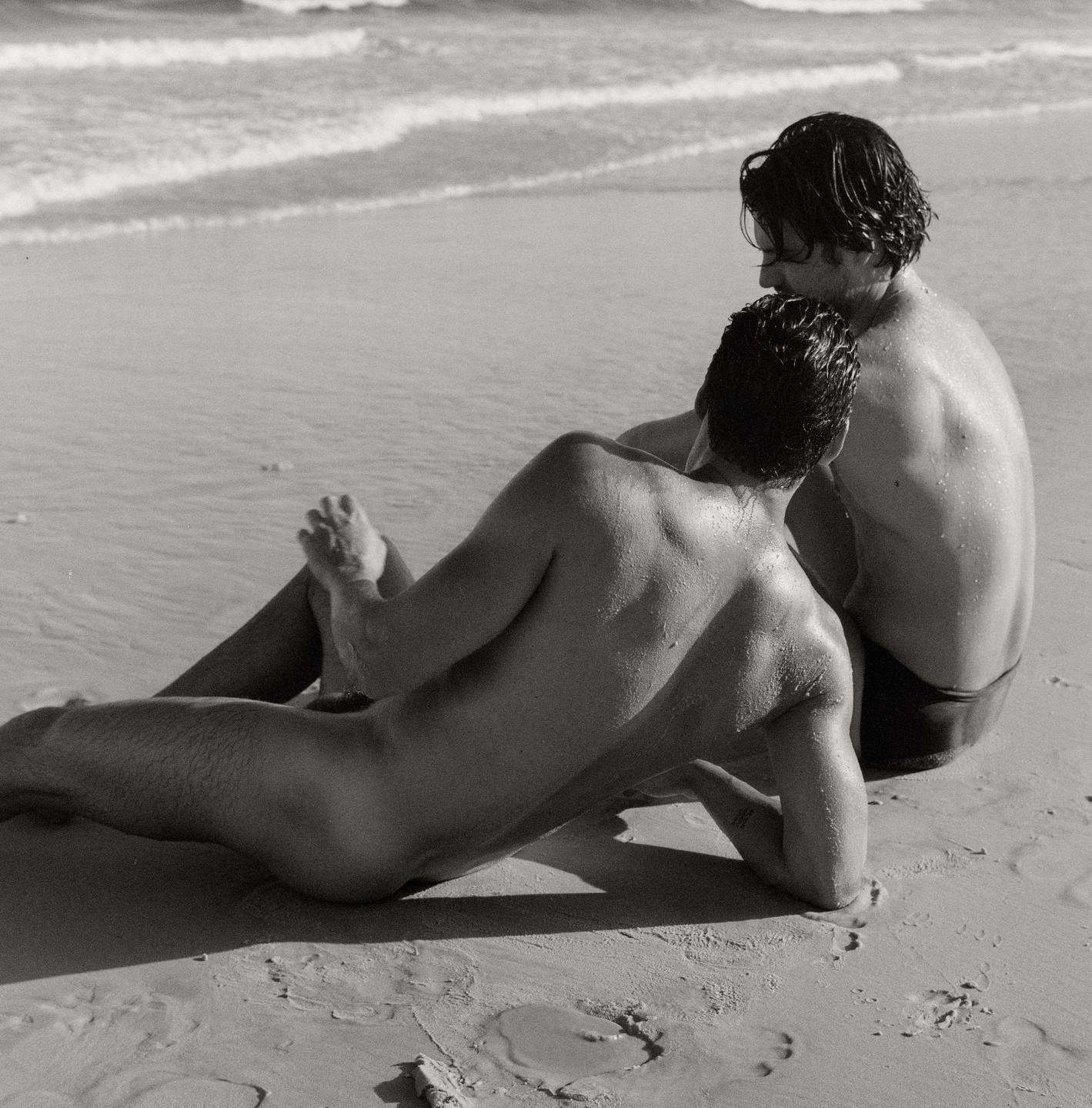 Two men are sitting on a sandy beach next to the ocean.