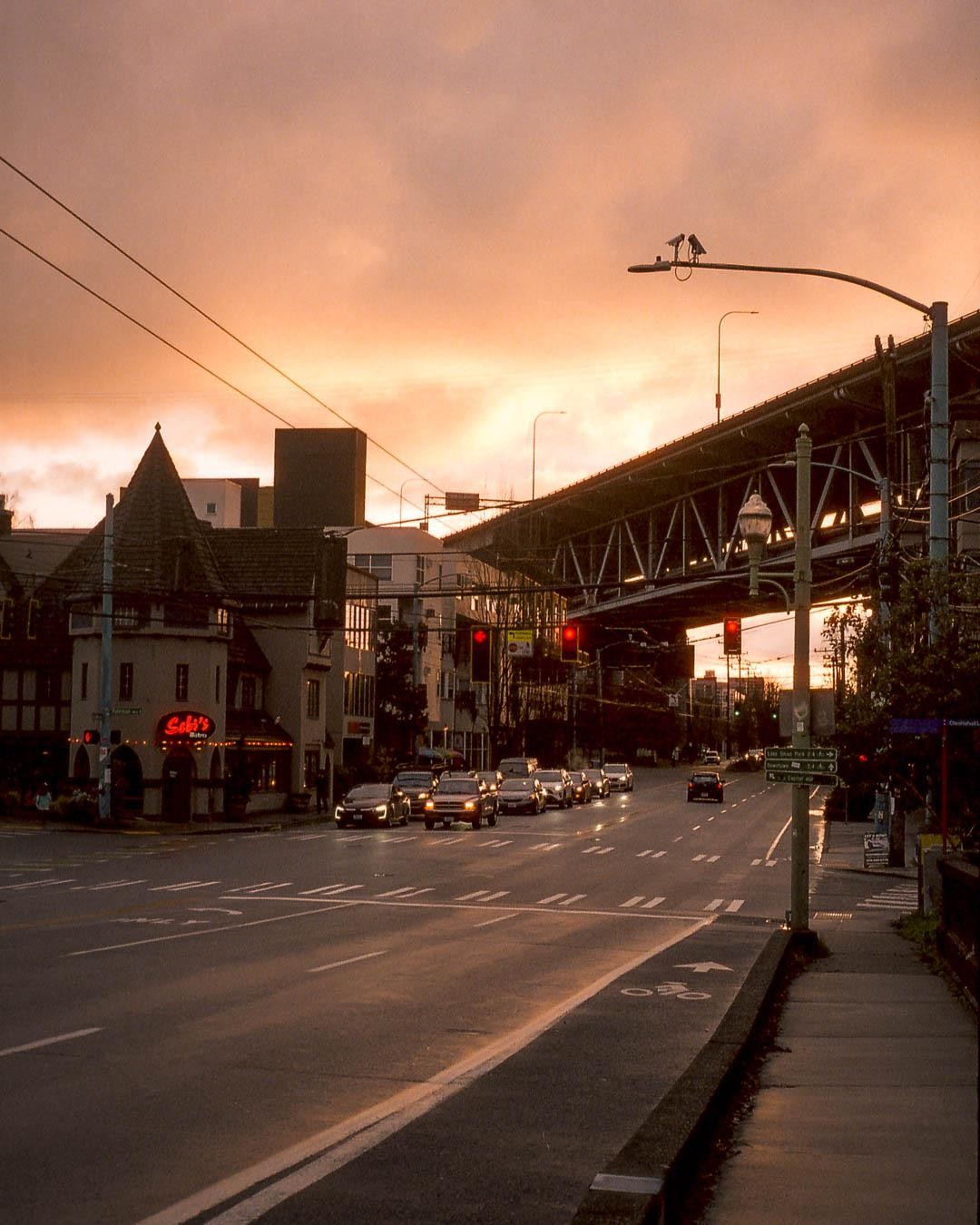 A street with cars and buildings is visible under a dramatic orange sky at dusk.