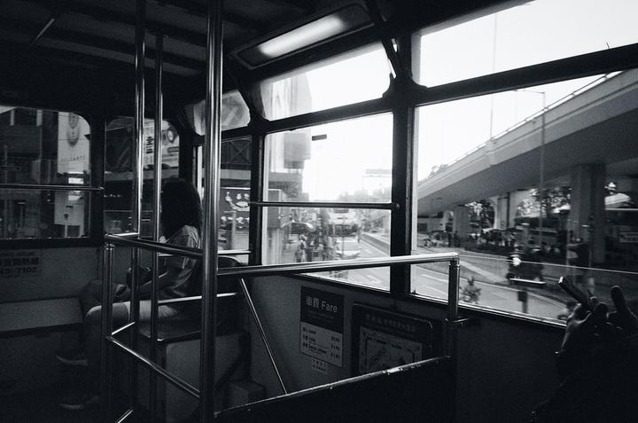 A woman sits inside a tram looking out the window at a street with an overpass.