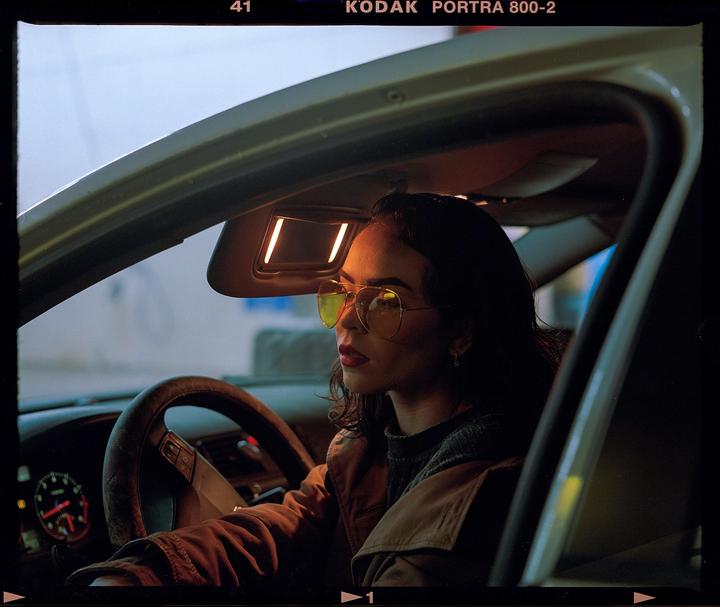 A woman wearing sunglasses sits in a car at night.