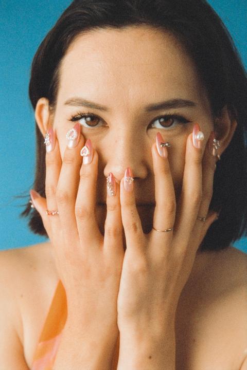 A woman covers her face with her hands, revealing her decorated fingernails.