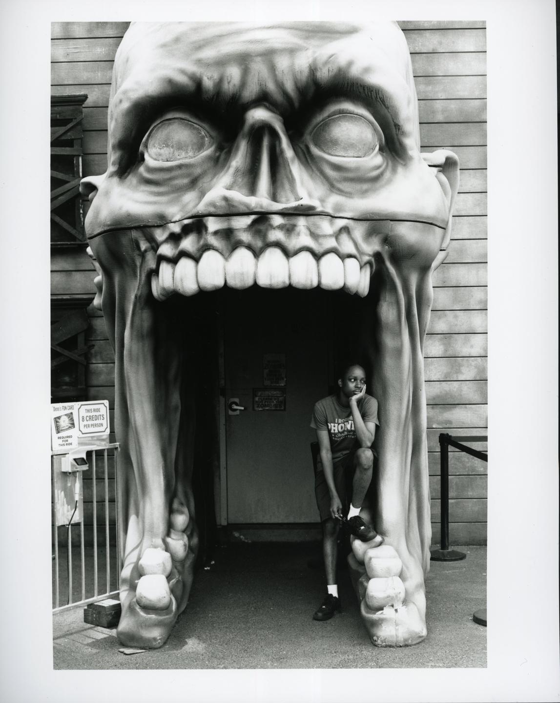 A man sits in the mouth of a giant skull sculpture.