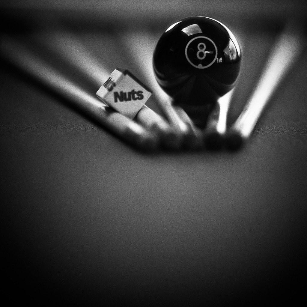 A black eight ball and a dice with the word "Nuts" are resting on a surface.