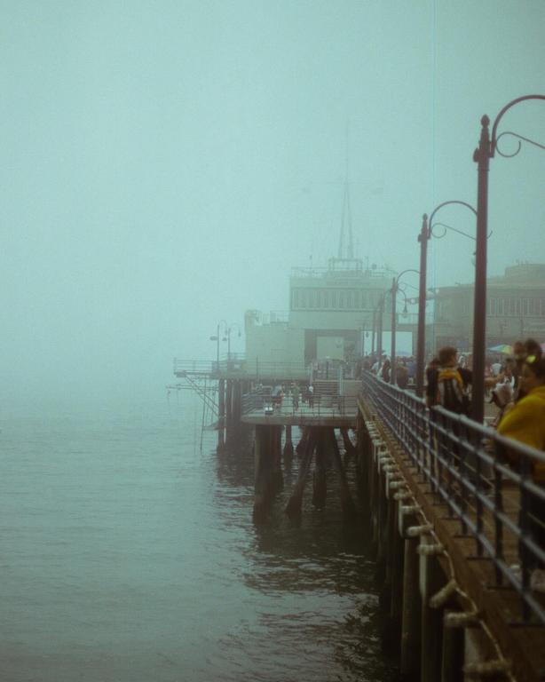 A pier extends into a hazy body of water with buildings visible in the distance.