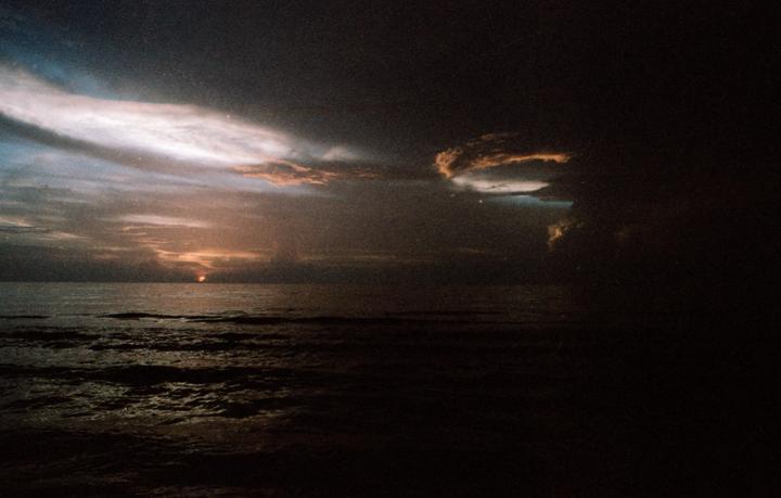 The sun rises over a dark ocean with storm clouds overhead.