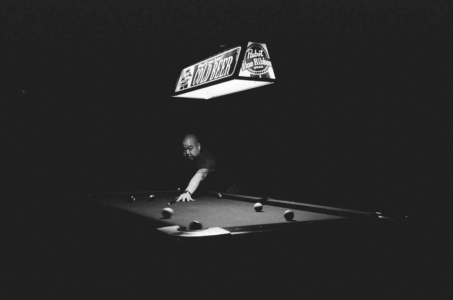 A man plays billiards under a "Cold Beer" sign.