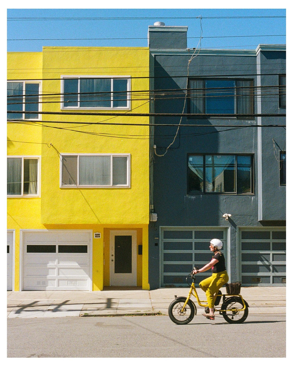 A woman on a yellow bicycle rides past a yellow and a gray building.