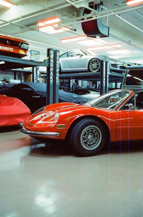 A red sports car is parked in a garage with other vehicles on lifts.