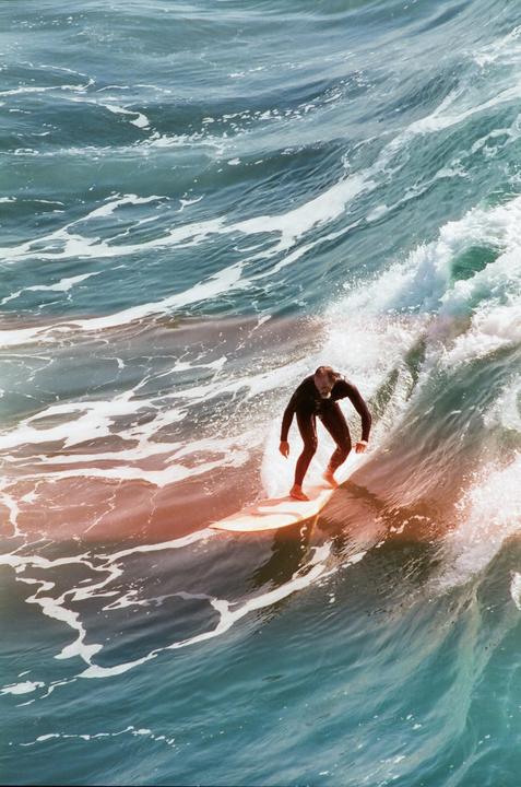 A surfer rides a wave with a light leak across the water.