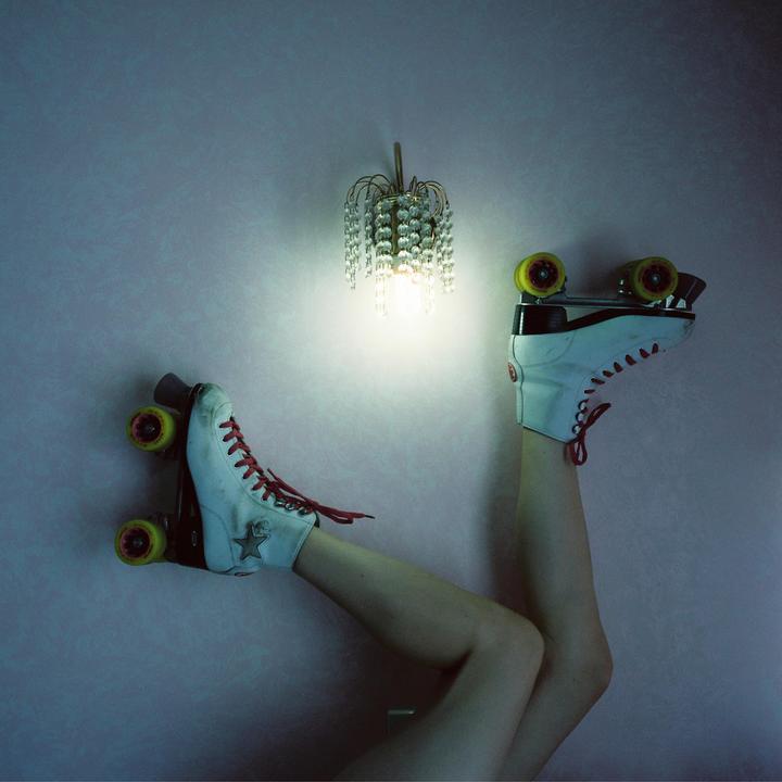 A person's legs wearing roller skates are raised against a pink wall with a lit sconce.