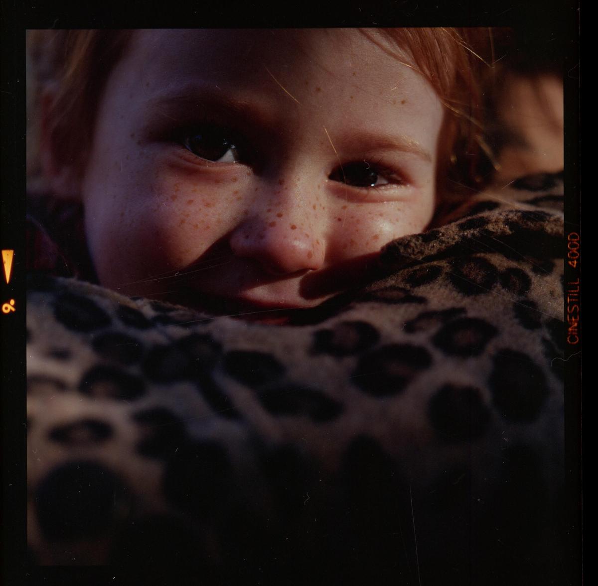 A child with freckles is partially covered by a leopard print blanket.