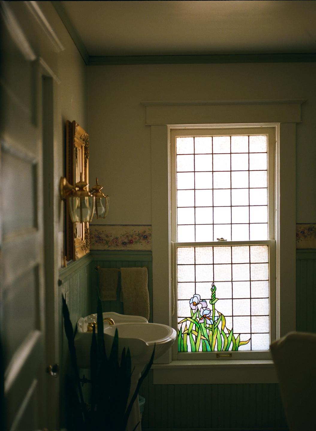A bathroom with a stained glass window depicting flowers is visible.