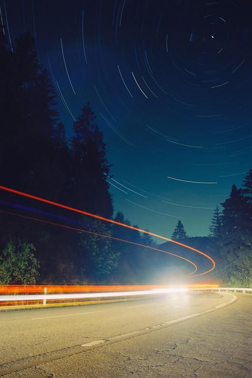 Light trails from vehicles on a winding road are visible under a night sky with star trails.