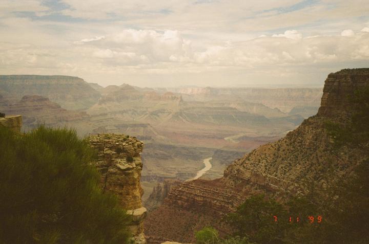 A river winds through a vast canyon under a cloudy sky.