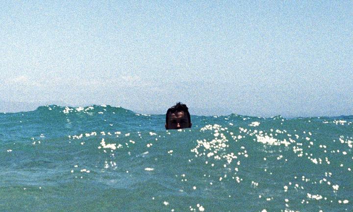 A man's head is visible above the surface of the ocean with sparkling water.