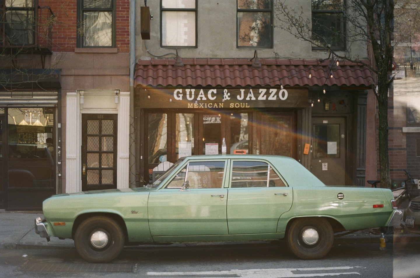 A light green car is parked on a street in front of a restaurant called Guac & Jazzo Mexican Soul.