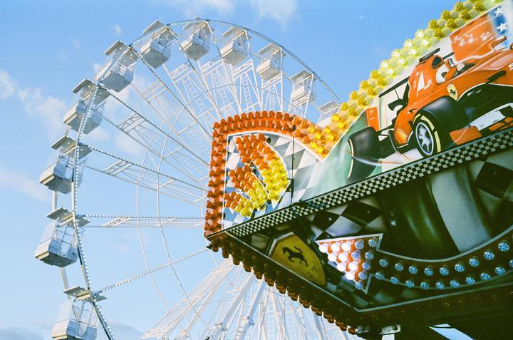 A ferris wheel and a funfair ride with a race car graphic are visible against a blue sky.