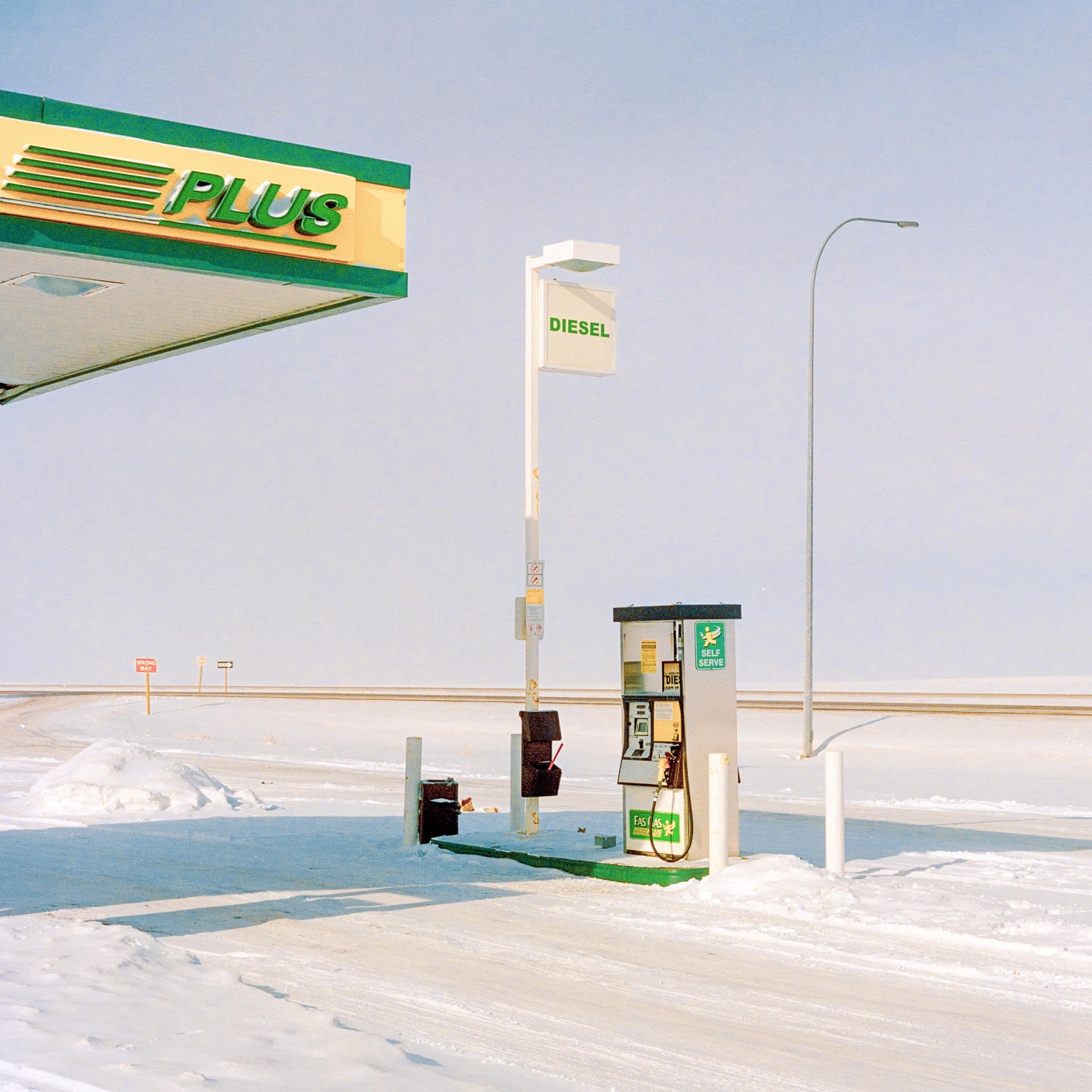 A gas station with a diesel pump stands in a snow-covered landscape under a clear sky.