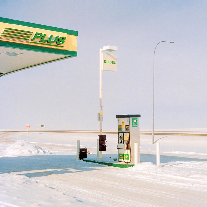 A gas station with a diesel pump stands in a snow-covered landscape under a clear sky.