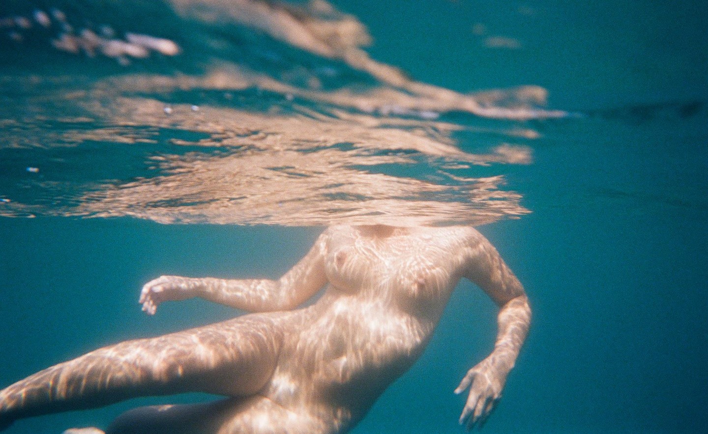 A woman floats underwater with light patterns visible on her body.