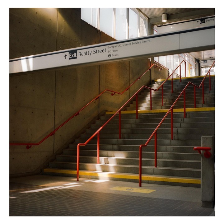 Sunlight illuminates a concrete staircase with red handrails and yellow safety strips.