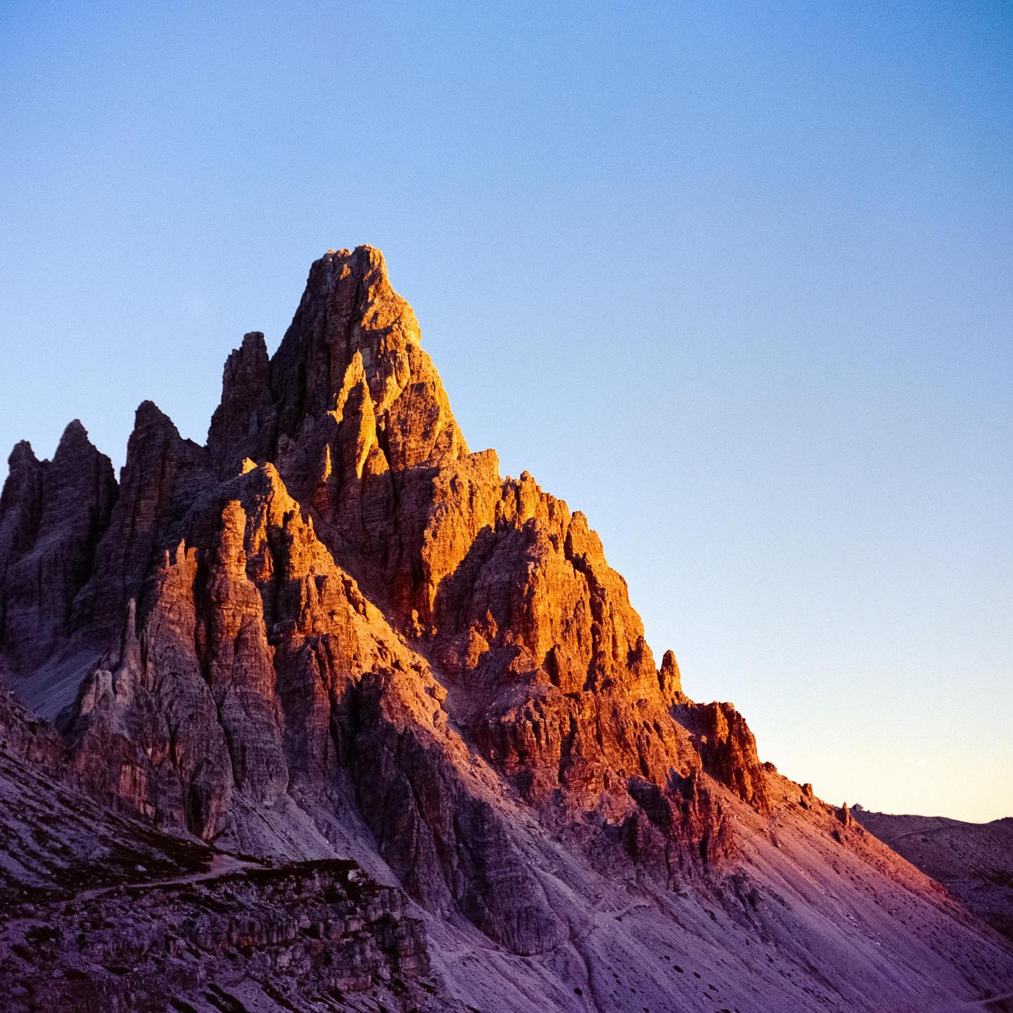 A mountain peak is illuminated by the golden light of sunrise against a clear sky.