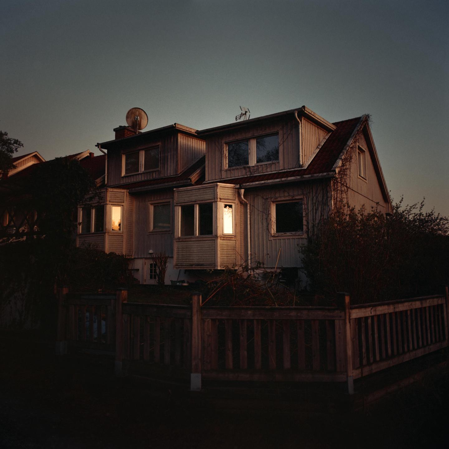 A large house with light shining from its windows is seen at dusk.