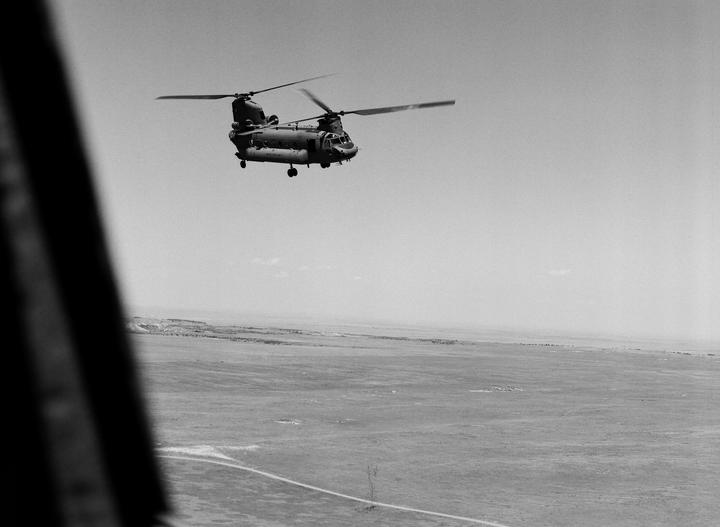 A helicopter flies over a vast, flat landscape with a road visible below.