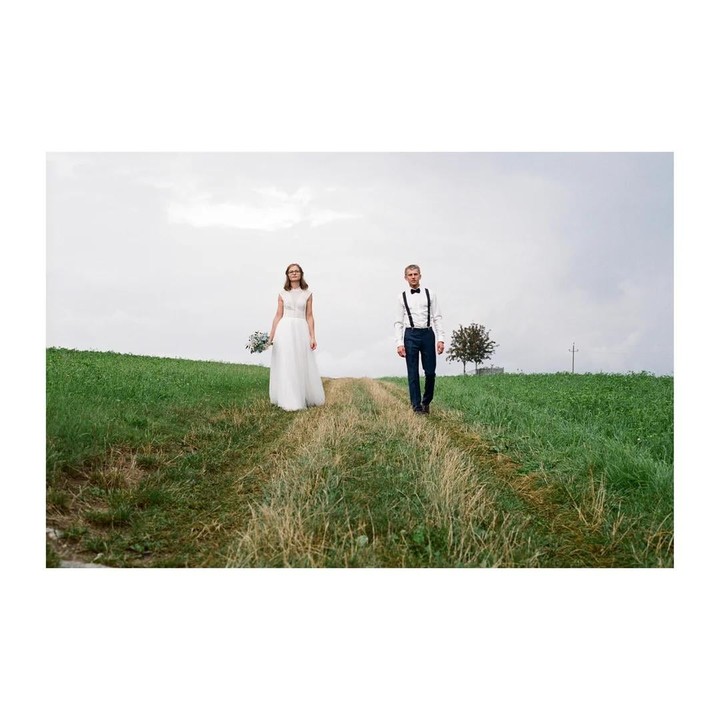 A couple walks on a grassy path in a field under a cloudy sky.