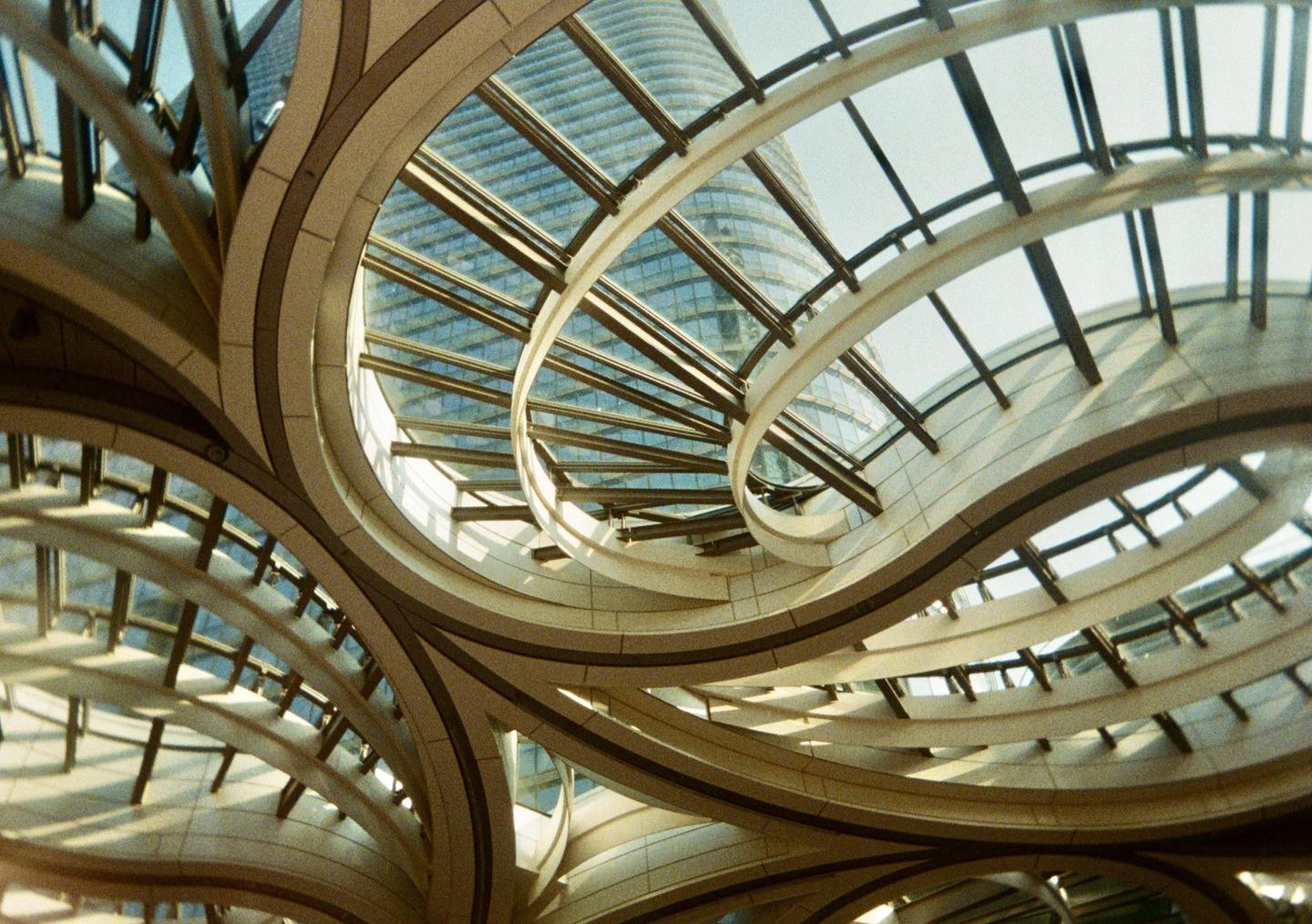 A low-angle view shows the curved beams and glass panels of a modern building's ceiling, with a skyscraper visible through the glass.