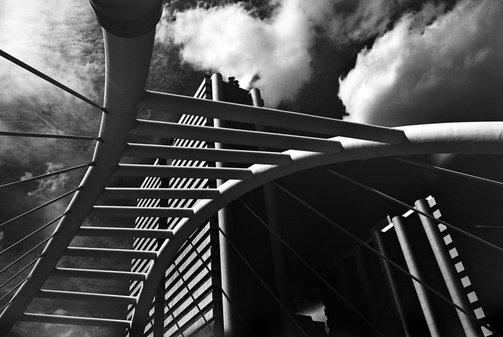 A low-angle view shows a modern building and bridge structure against a cloudy sky.