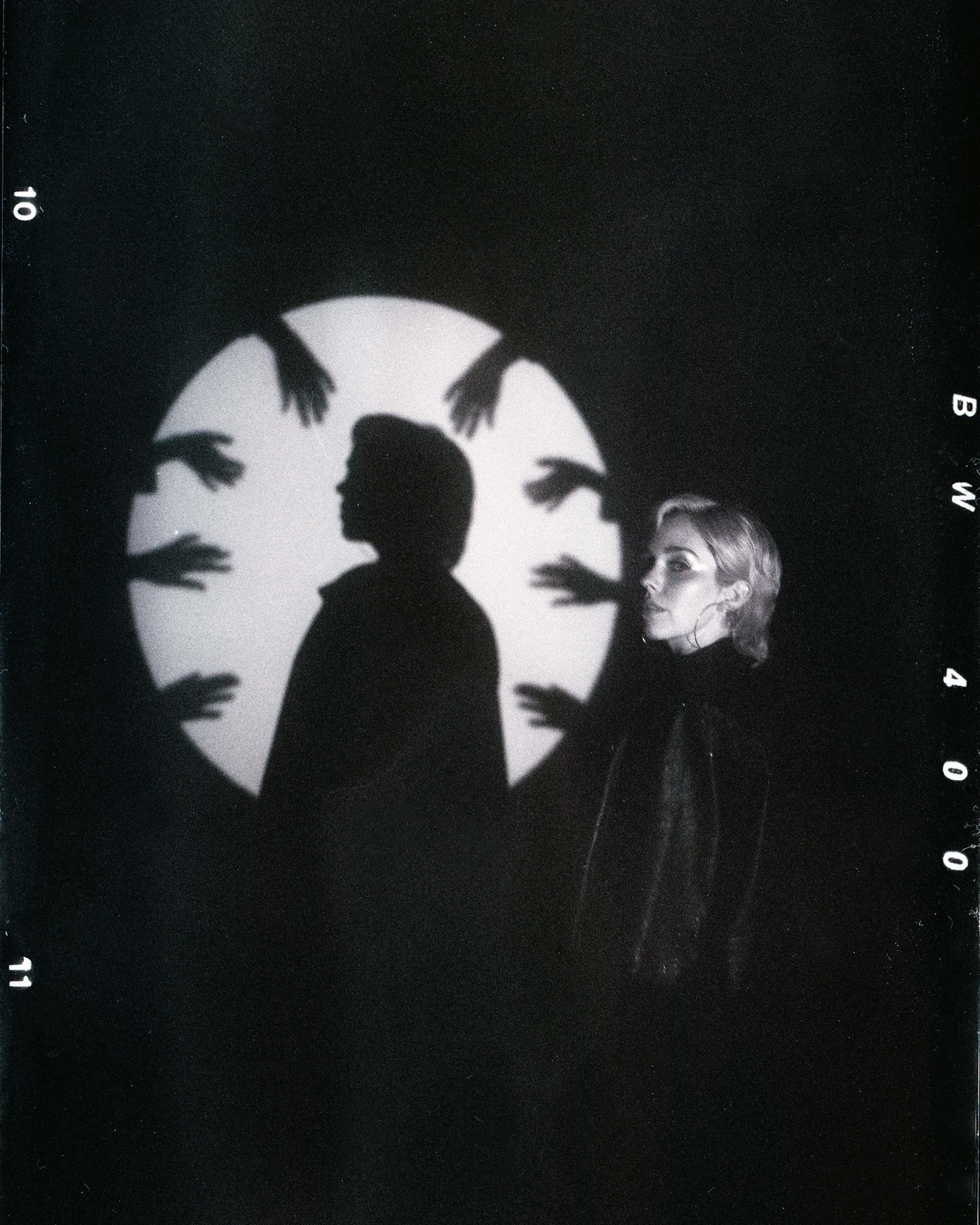 A woman stands next to a large circular light with a silhouette of a person and multiple hands projected onto it.