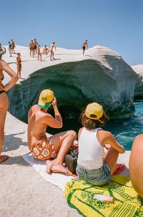 A group of people are relaxing on a white rock formation next to the ocean under a clear blue sky.