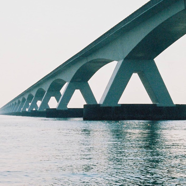 A long bridge with many arches stretches across a body of water under a bright sky.