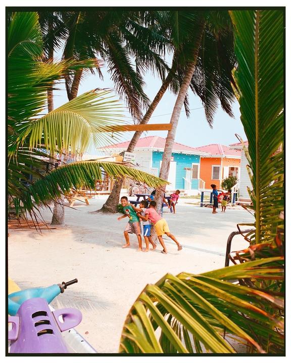 Children play on a sandy beach surrounded by palm trees and colorful buildings.