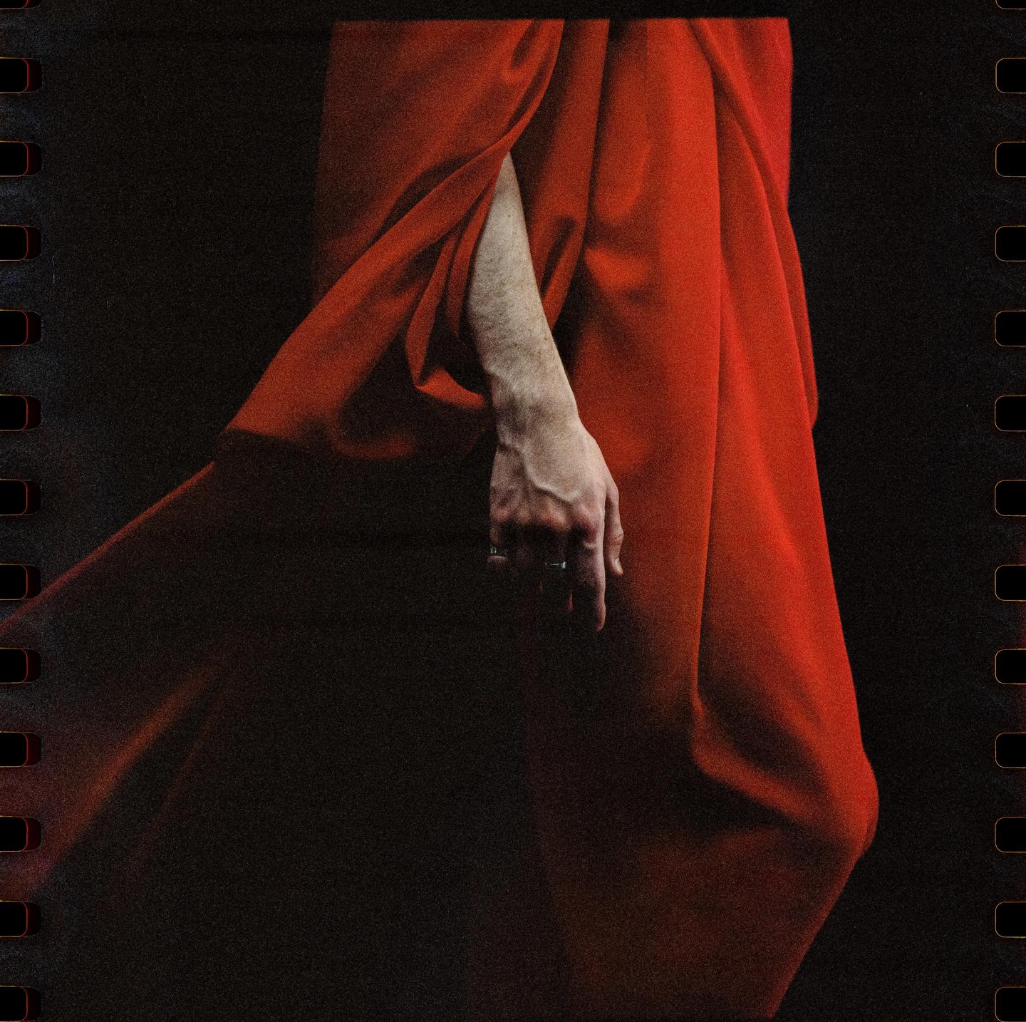 A person's arm and hand are visible against a red draped fabric.