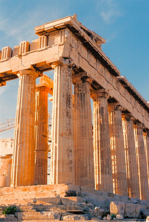 The Parthenon is illuminated by golden hour light against a clear blue sky.