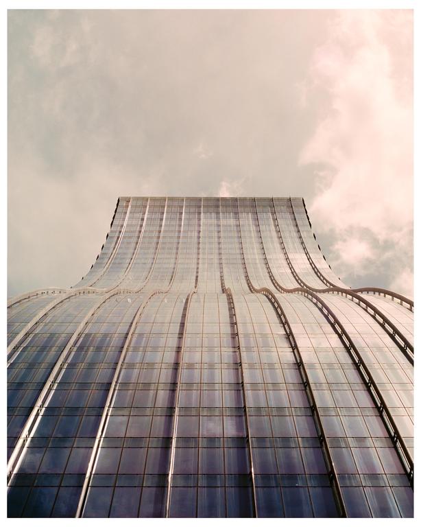 A tall, wavy glass building with a cloudy sky in the background is shown from a low angle.
