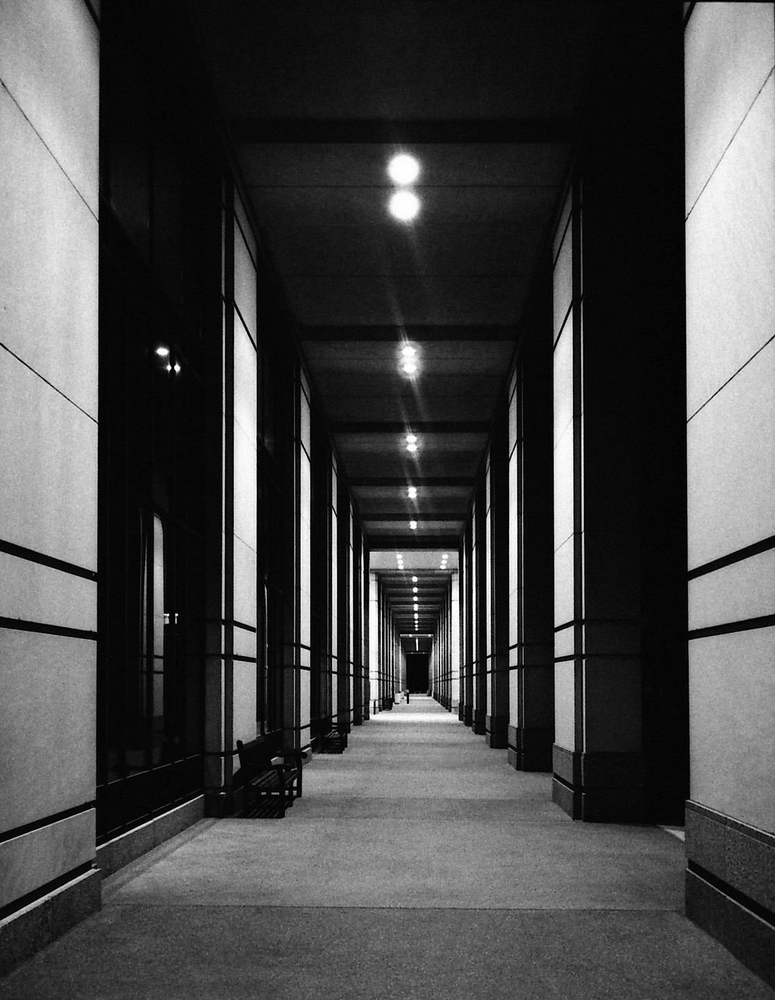 A long, empty hallway with benches on the left and lights on the ceiling stretches into the distance.