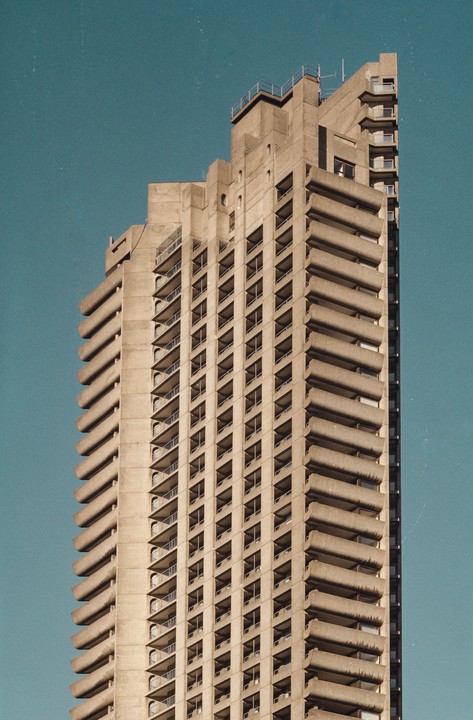 A tall concrete building with many balconies stands against a clear blue sky.