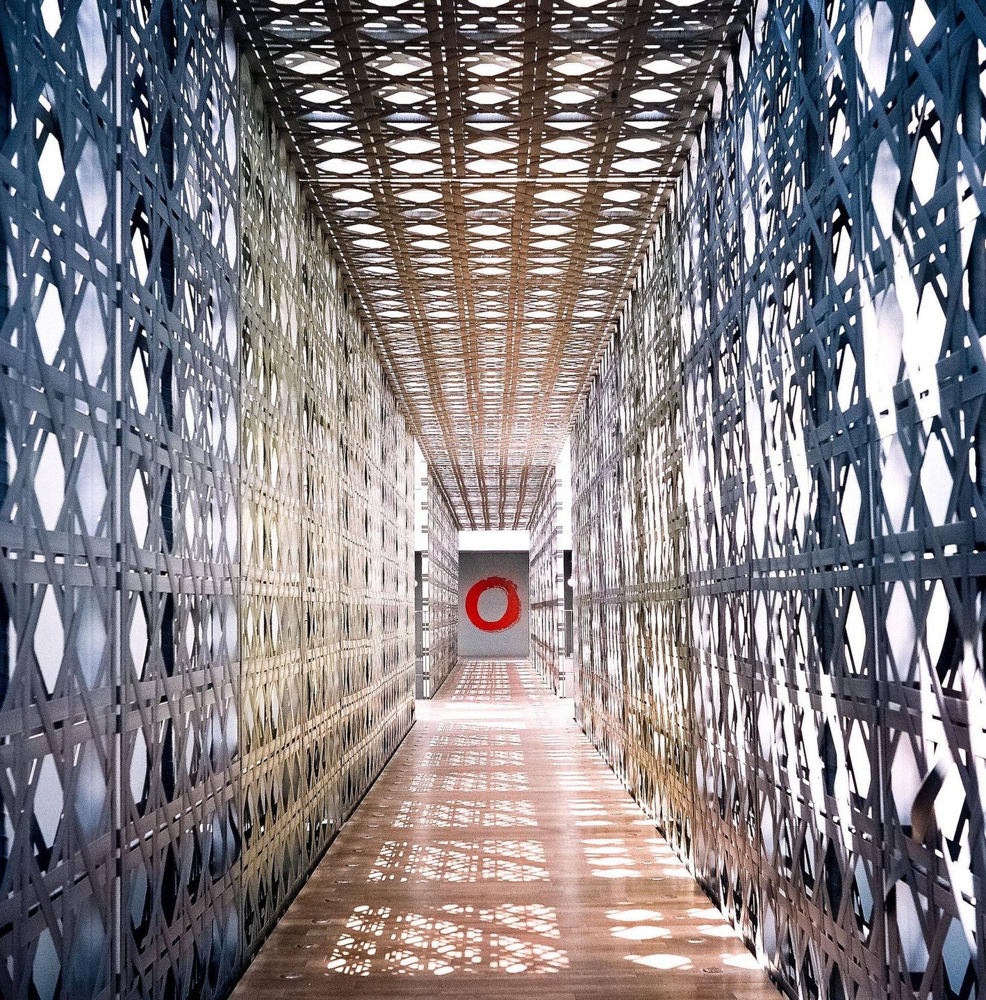 A long, narrow hallway with patterned walls and ceiling leads to a red circle on a far wall.